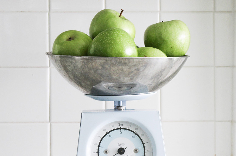 Being diagnosed with Fibromyalgia. Photo shows green apples being weighed on a scale. The background is square, white tiles.