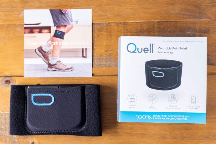 Photo shows the Quell inside a pocked on the sports band, a Quell leaflet and box that reads "wearable pain relief technology, 100% drug-free relief from chronic pain".