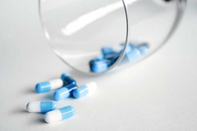 Photo shows a glass on its side with blue and white pills spilling out.