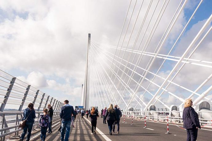 Photograph shows people walking over the Queensferry Crossing with the support tower and cables to the right.
