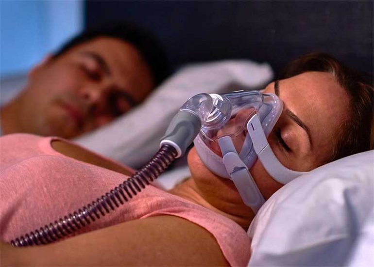 Learn about the connection between sleep apnea and Fibromyalgia and how treatment can help to improve your quality of life. Image shows a woman sleeping wearing a CPAP machine.