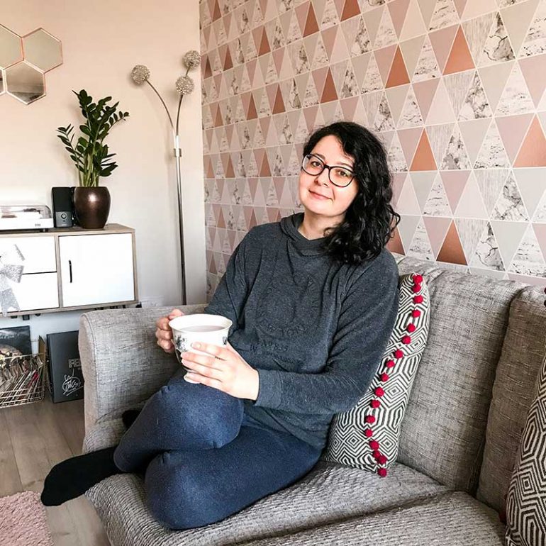 Photo shows me sitting on my sofa with a cup of tea. In this post, I share what my experience was like going through a healing crisis after ACT treatment at Infusio.