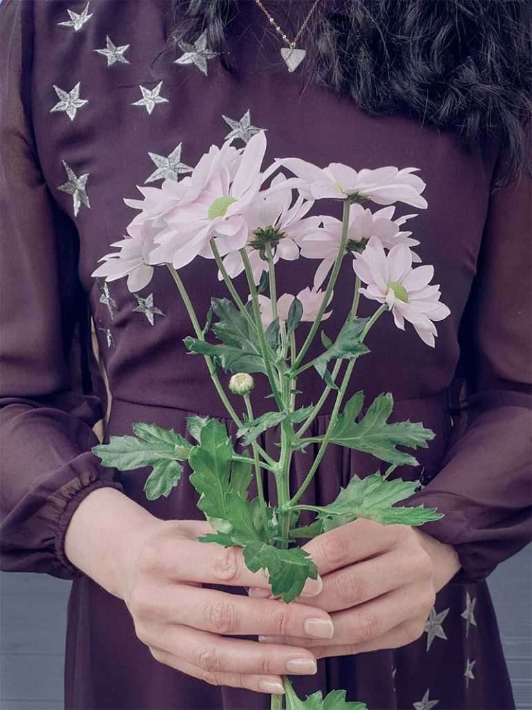 A close up of Donna's hands holding pink flowers. Donna is wearing a burgundy dress with silver stars that can be seen behind the flowers.