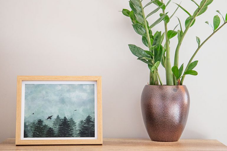 Photo of a forest watercolour print I am selling on Etsy in a frame next to a plant.
