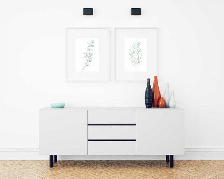 Two eucalyptus watercolour paintings framed behind a white sideboard.