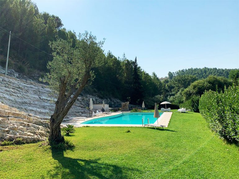 Swimming pool at our Giarratana accommodation surrounded by grass, greenery with a stone backdrop.