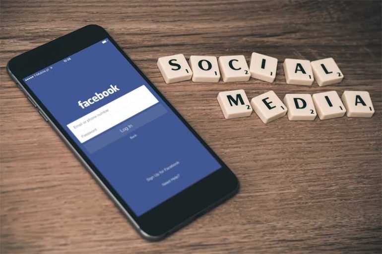 Photo shows a mobile phone on a desk displaying the facebook log in page. Next to it are scrabble letters that read 'social media'