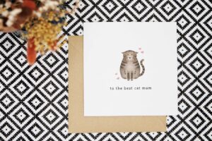 A cute card with a tabby cat sitting with its eyes closed and ears down looking content. There are four pink hearts around the cat and the card reads to the best cat mum.