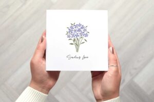 Photo shows the sympathy card being held. There is a bunch of illustrated forget me not flowers. Underneath are the words sending love in a calligraphy font.