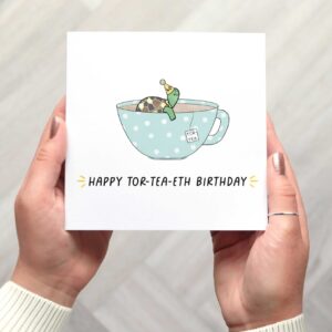 40th birthday card features a cute illustrated tortoise sitting in a teal tea cup with white polka dots. It wears a yellow party hat with 40 on it. There is a tor-tea label from a tea bag hanging on the side and the words happy tor tea eth birthday