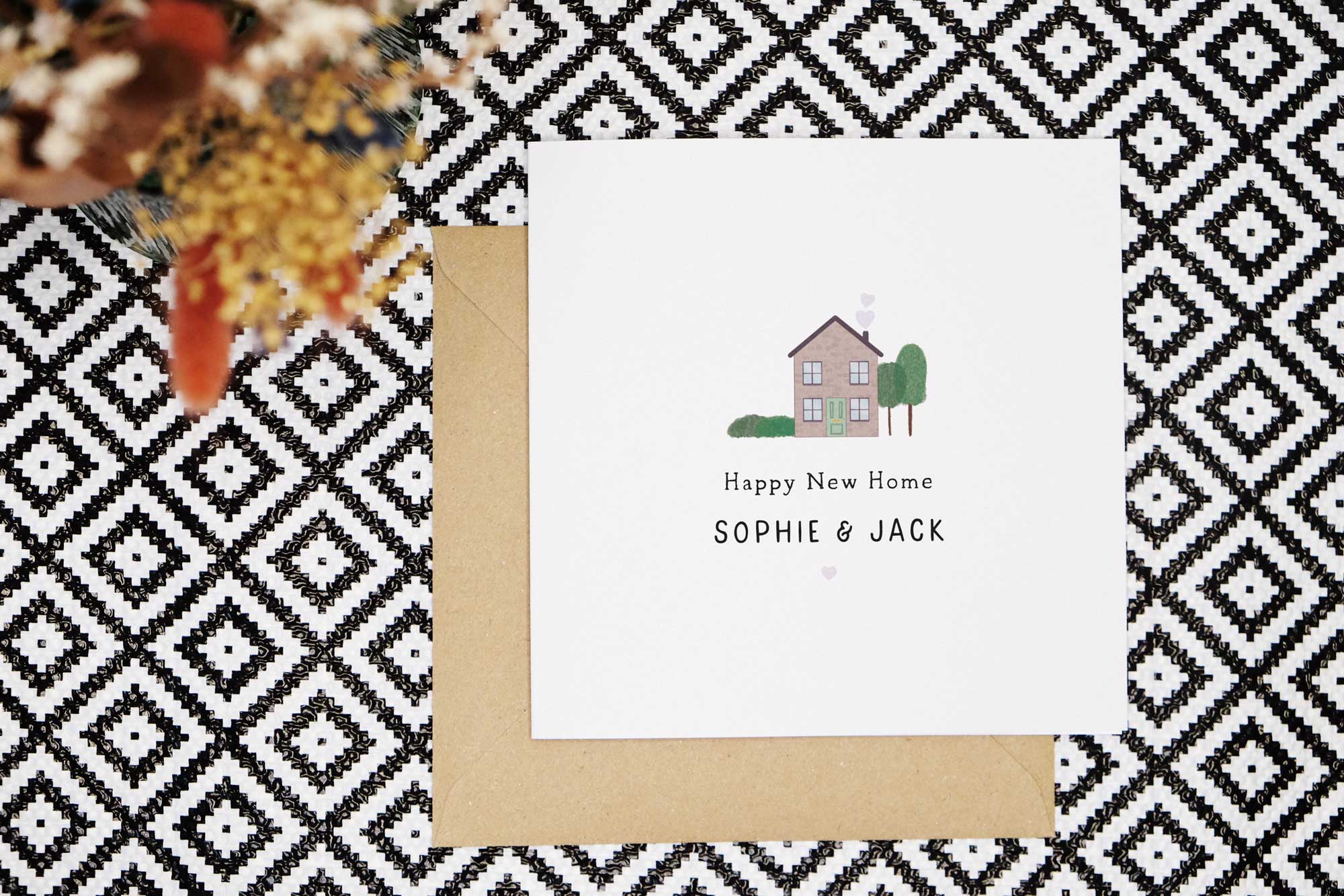 This housewarming card featuring an illustration of a two storey brick house with a green door, hedge and tree. Underneath are the words Happy New Home. Names can be personalised on the front of the card also. There is a small heart beneath the text.
