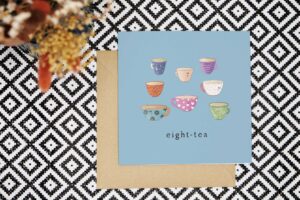 This pun 80th card has a light blue background and features eight illustrated cups of tea, each of a different type, colour and pattern. They all have cute smiling faces. The card reads eight tea.