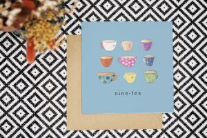 This pun 90th card has a light blue background and features nine illustrated cups of tea, each of a different type, colour and pattern. They all have cute smiling faces. The card reads nine tea.