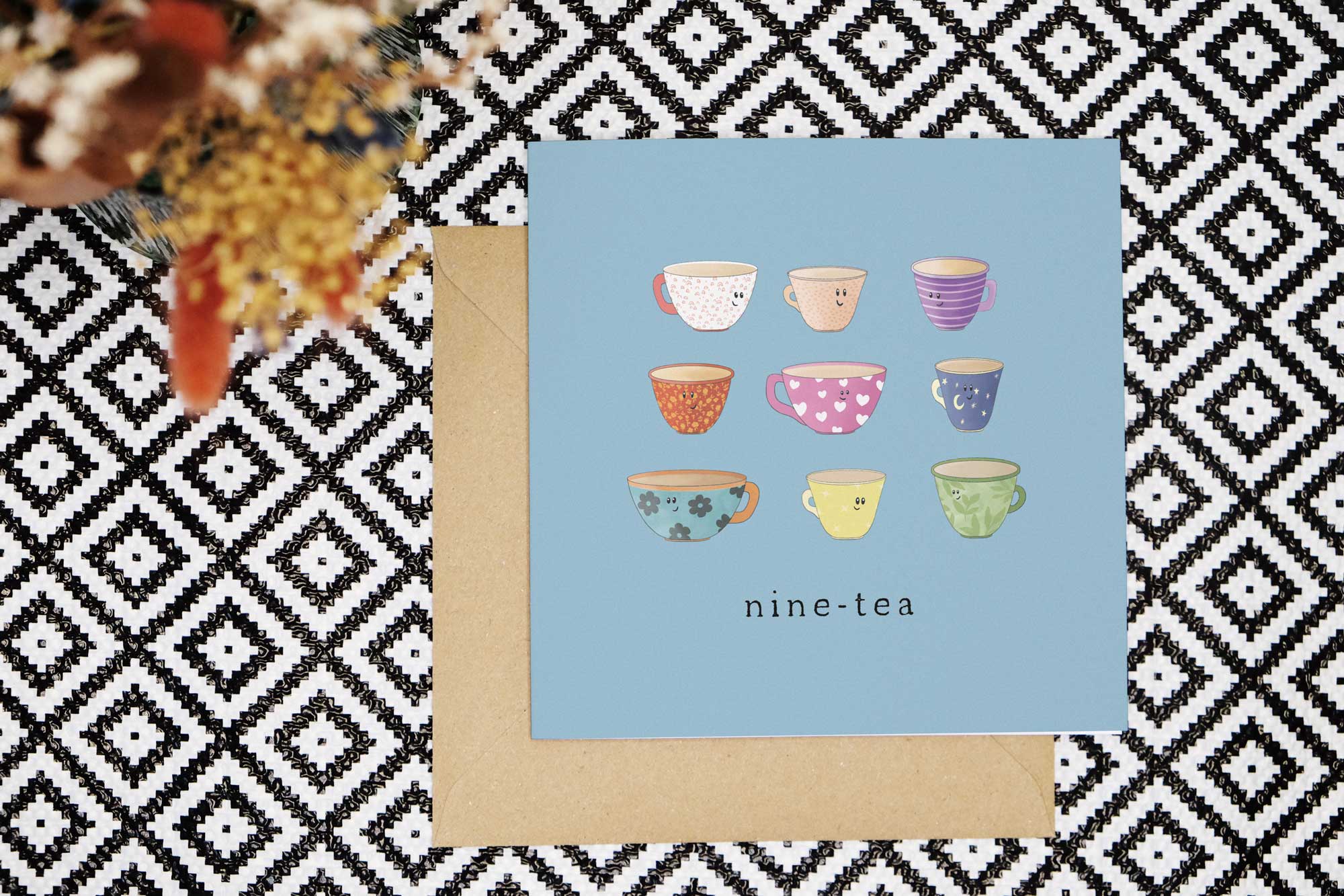 This pun 90th card has a light blue background and features nine illustrated cups of tea, each of a different type, colour and pattern. They all have cute smiling faces. The card reads nine tea.