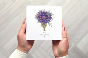 Sympathy card with an illustrated floral bouquet of lavender, pink roses, yellow flowers and botanicals wrapped in grown paper and tied with string. The card reads with deepest sympathy with a small pink heart under the text.