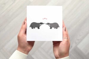This cute valentines day card features two illustrated badgers stood looking at each other with three small pink love hearts above their heads.