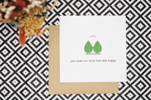 This cute pun love card features two illustrated smiling leaves holding hands with love pink hearts above their heads and the words you make me unbe-leaf-ably happy