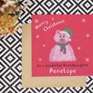 This personalised Christmas card features a hand drawn red background and polar bear wearing a green striped scarf and a green Santa hat with white trim and pom pom. Created using oil pastels and embellished with hand drawn digital snowflakes. The card reads Merry Christmas to a wonderful and can be personalised with the relation and name
