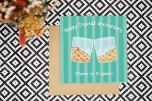 Celebrate 15 years married with this colourful and playful card with two clinking crystal whiskey glasses. The card has a green striped background and the card reads Happy Crystal Anniversary Cheers to 15 years